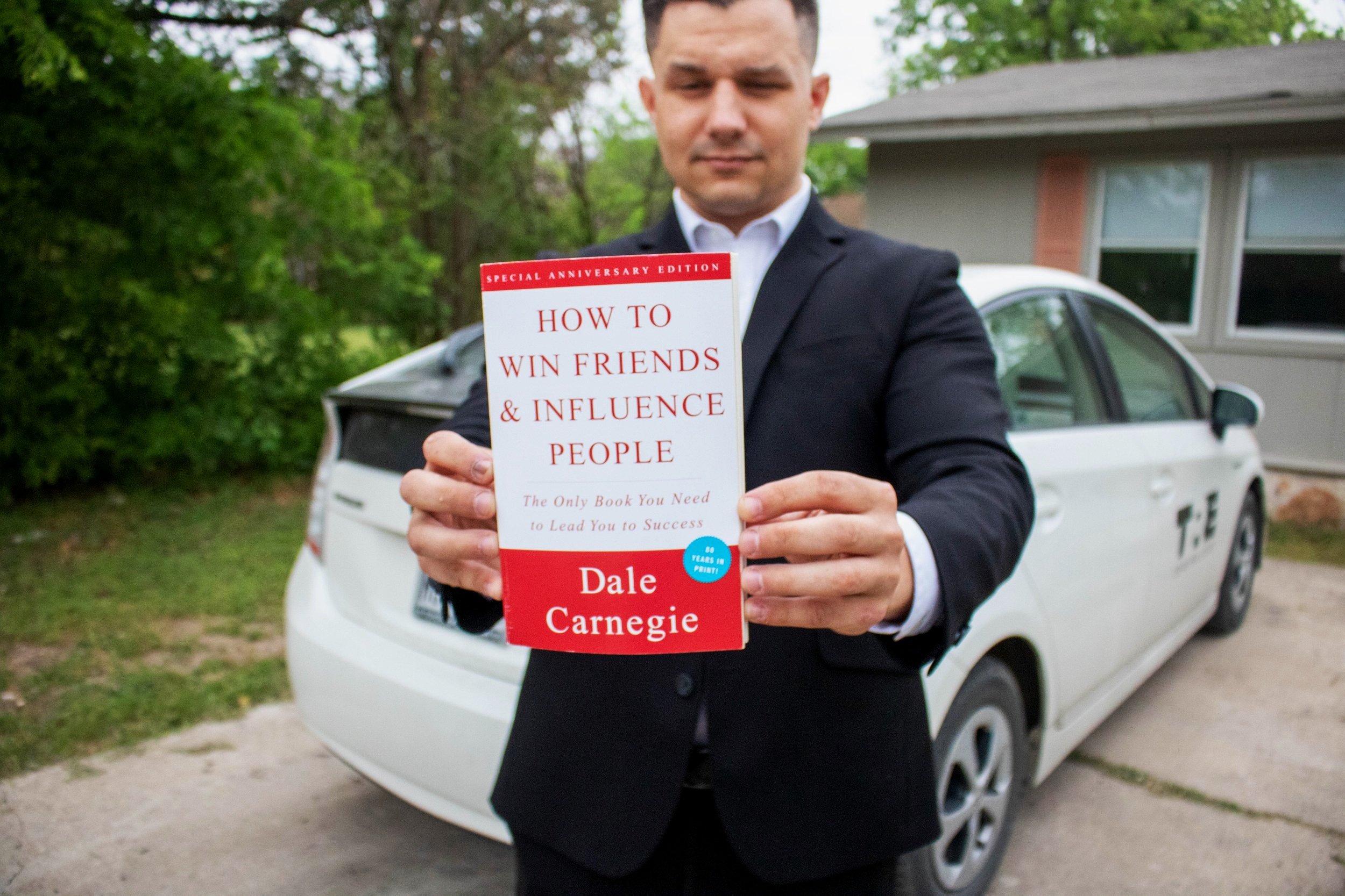Man in black suit holding the book, how to win friends and influence people